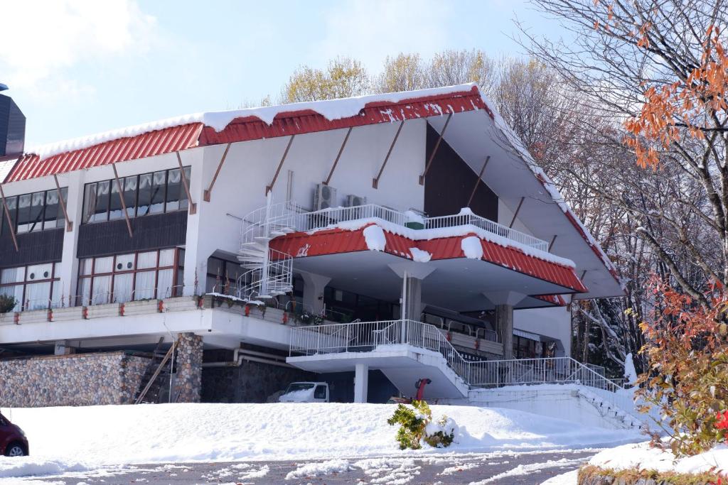 Un edificio blanco con nieve en el suelo. en Kurohime Kogen Hotel, en Shinano
