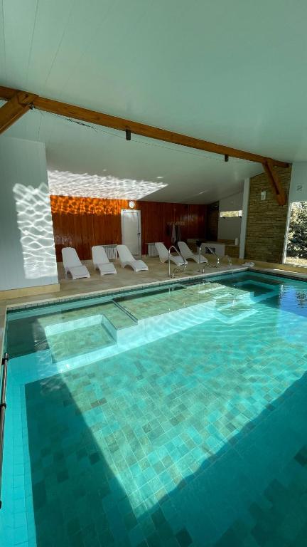 a large swimming pool in a hotel with white chairs at Las Nubes Piscina interior y exterior in El Bolsón