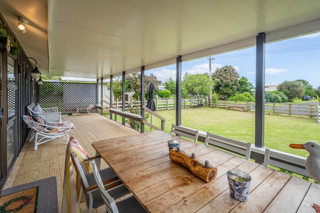 a porch with a wooden table and a large window at Hosts on the Coast Paws & Relax Bach in Hahei