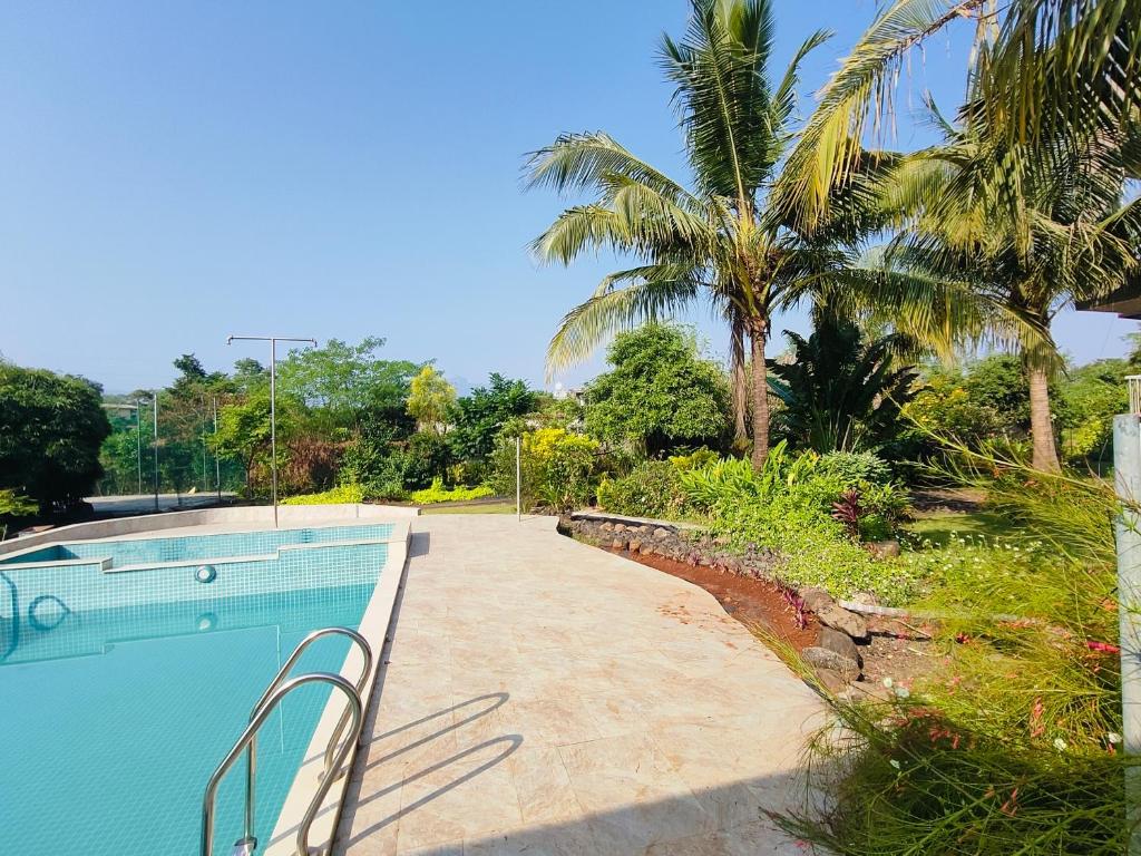a swimming pool with palm trees in the background at Green Courtyard Luxury Villa in Badlapur