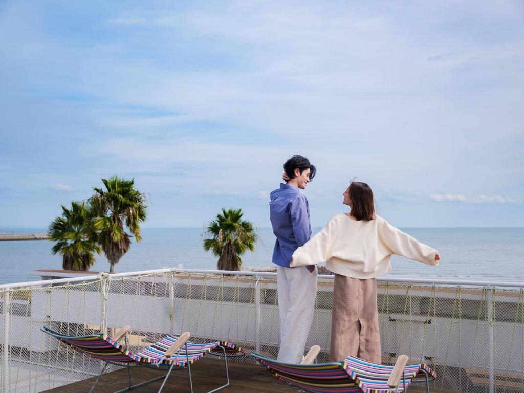 a man and a woman standing on a balcony overlooking the ocean at そらすな Beach Side Resort Hotel in Yukuhashi