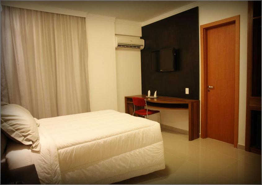 een slaapkamer met een bed, een bureau en een televisie bij Atlântico Golden Apart Hotel in Santos