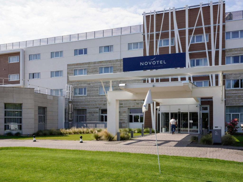 a building with a man walking in front of it at Novotel Saint-Quentin en Yvelines in Magny-les-Hameaux