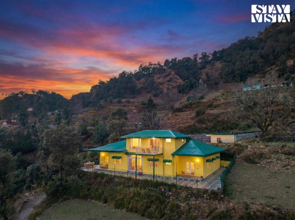 una vista dall'alto di una casa gialla con un tetto verde di StayVista at Cloudview Villa with Valley view, WiFi & BBQ a Mussoorie
