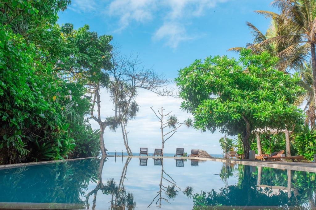a swimming pool with trees and chairs in the water at Roman Beach Hotel in Hikkaduwa