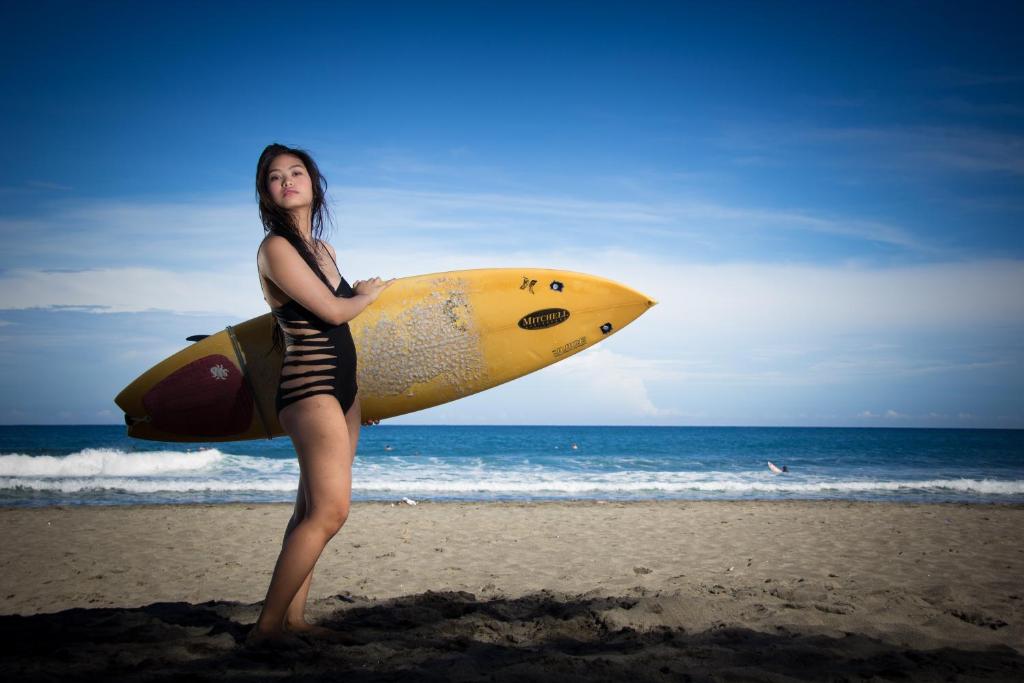 una mujer parada en la playa sosteniendo una tabla de surf en Scenic View Tourist Inn, en San Juan