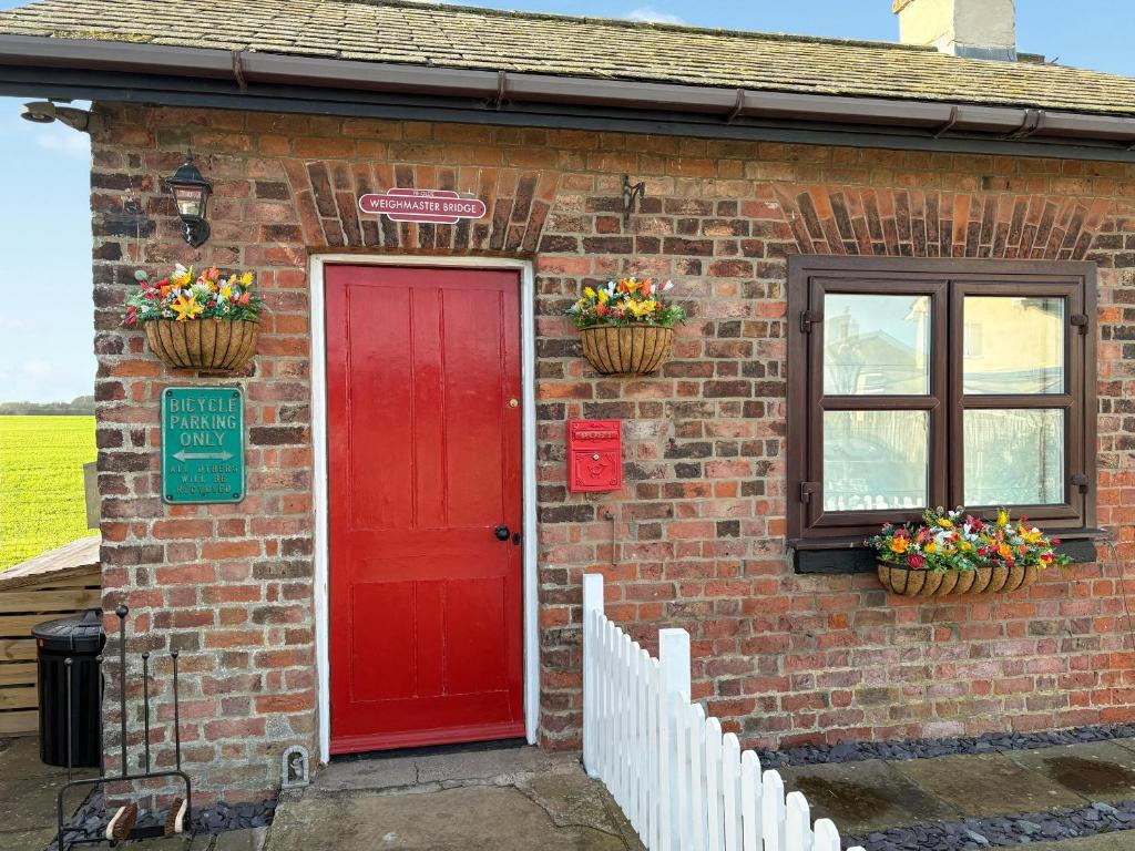 Una casa de ladrillo con una puerta roja y dos cestas de flores. en The Old Weighbridge, en Fulstow