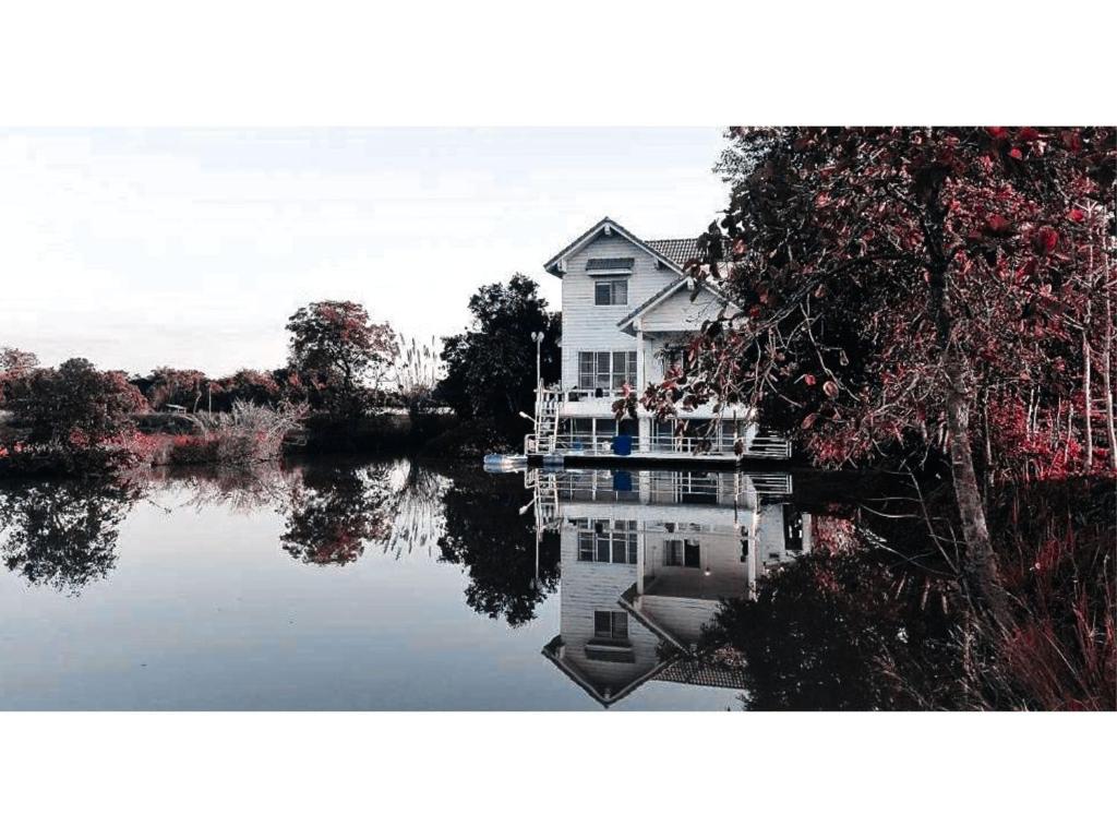 a house sitting on a lake with its reflection in the water at black & white rice camp แบล็กแอนด์ไวต์ไรซ์แคมป์ 