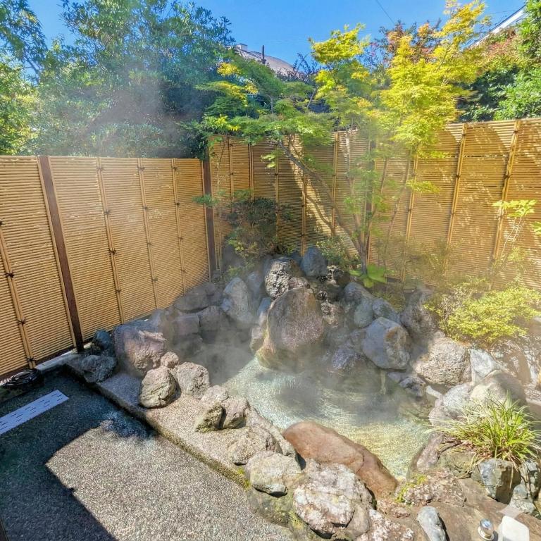 a hot spring in a garden with rocks and a fence at Private Open-air Onsen Sakura Cottage Izukogen in Ito
