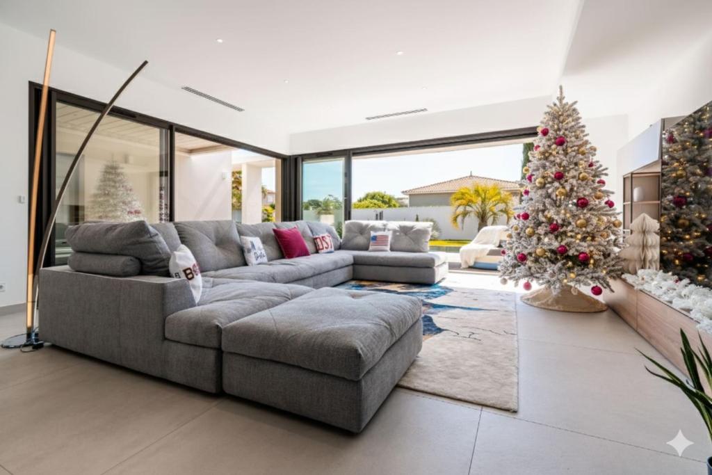 een woonkamer met een grijze bank en een kerstboom bij Villa Boston luxury home with pool and Cali vibes in Le Grau-dʼAgde