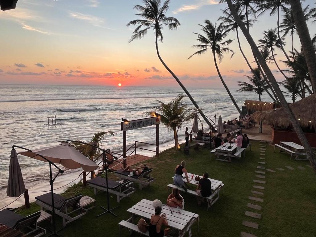 people sitting at tables on the beach at sunset at Kabalana Surf Hostel in Ahangama