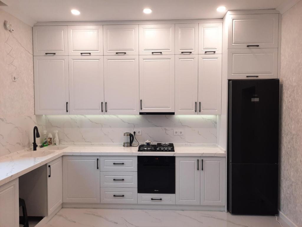 Una cocina con gabinetes blancos y un refrigerador negro. en Уютный дом для семьи AL INN, en Qusar