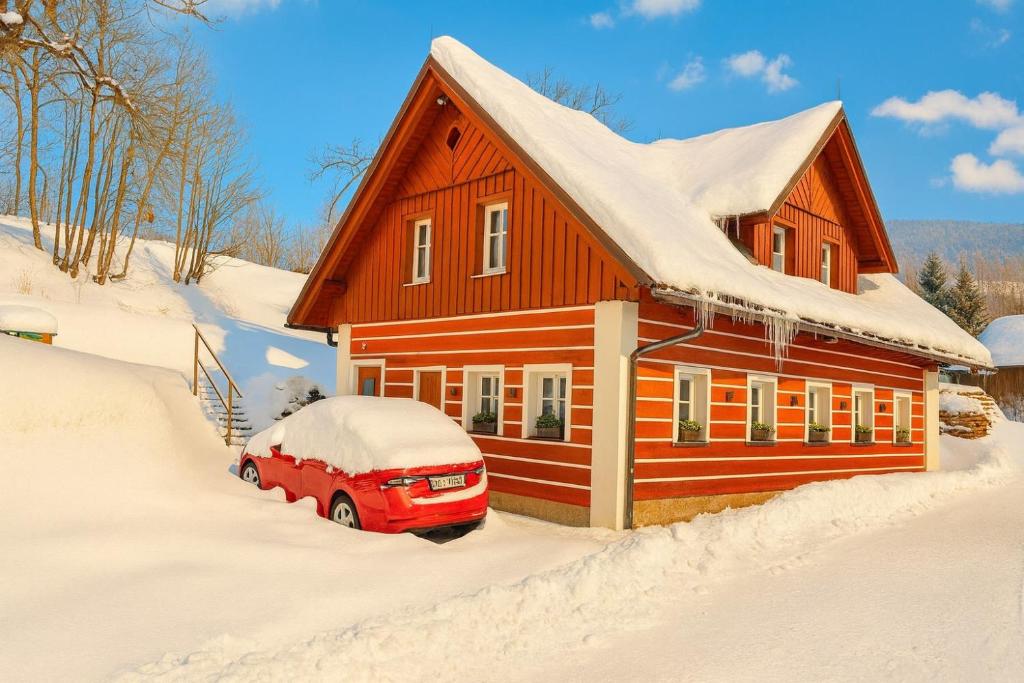 uma casa vermelha com um carro estacionado na neve em Apartmány mlýn em Rokytnice nad Jizerou