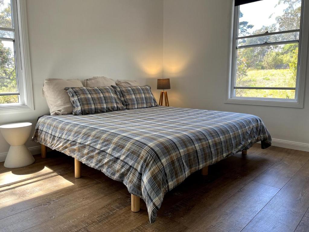 a bedroom with a bed with a plaid blanket and two windows at Happy Mountain House in Blackheath