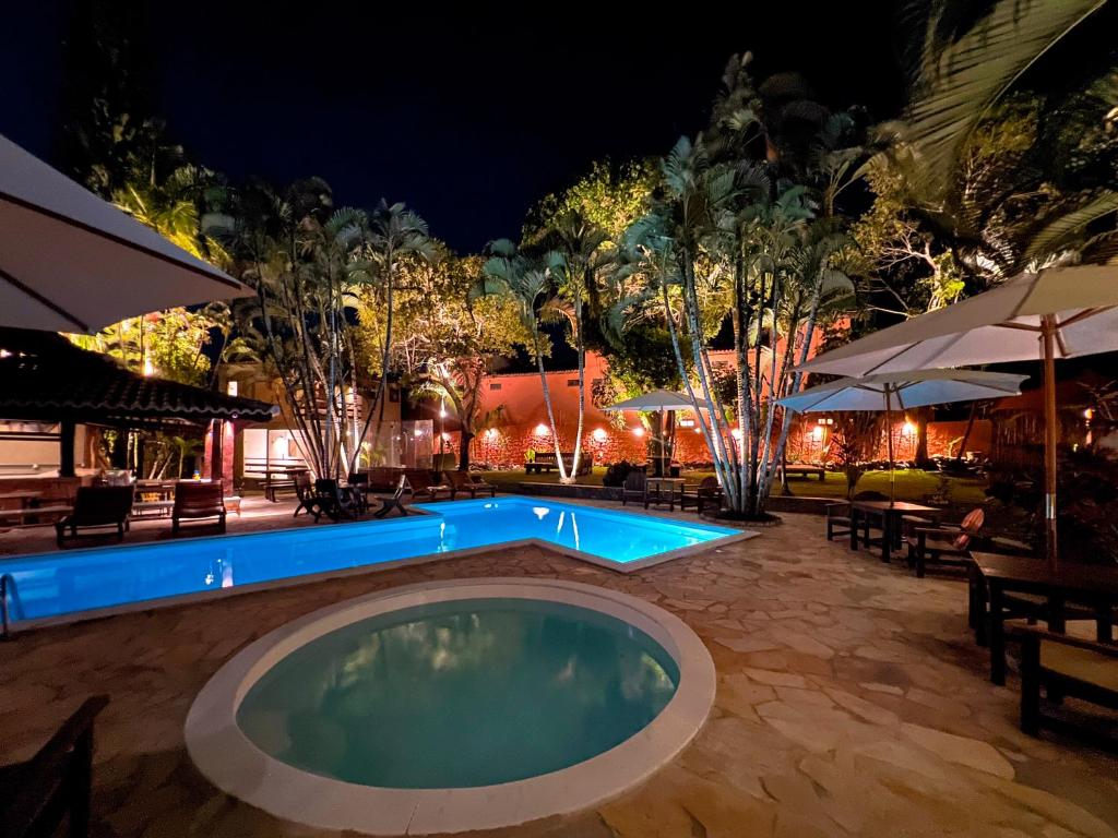a swimming pool at night with tables and umbrellas at Pousada Arraial Candeia in Arraial d'Ajuda