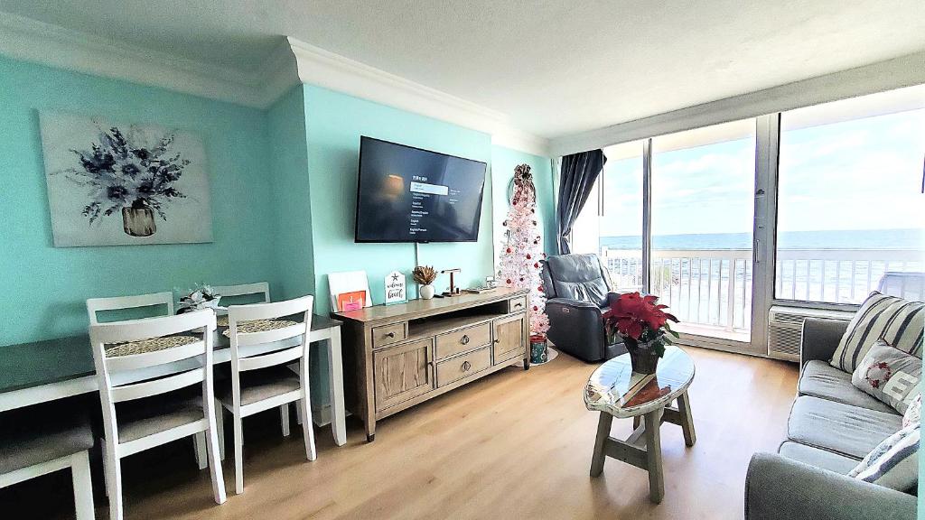 Sunkissed-Modern Oceanfront Condo Daytona Beach في دايتونا بيتش: غرفة معيشة مع تلفزيون وطاولة وكراسي