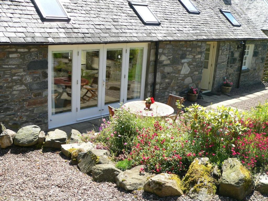 Cosy cottage for two in the highlands في Fortingall: منزل حجري مع فناء مع طاولة وزهور
