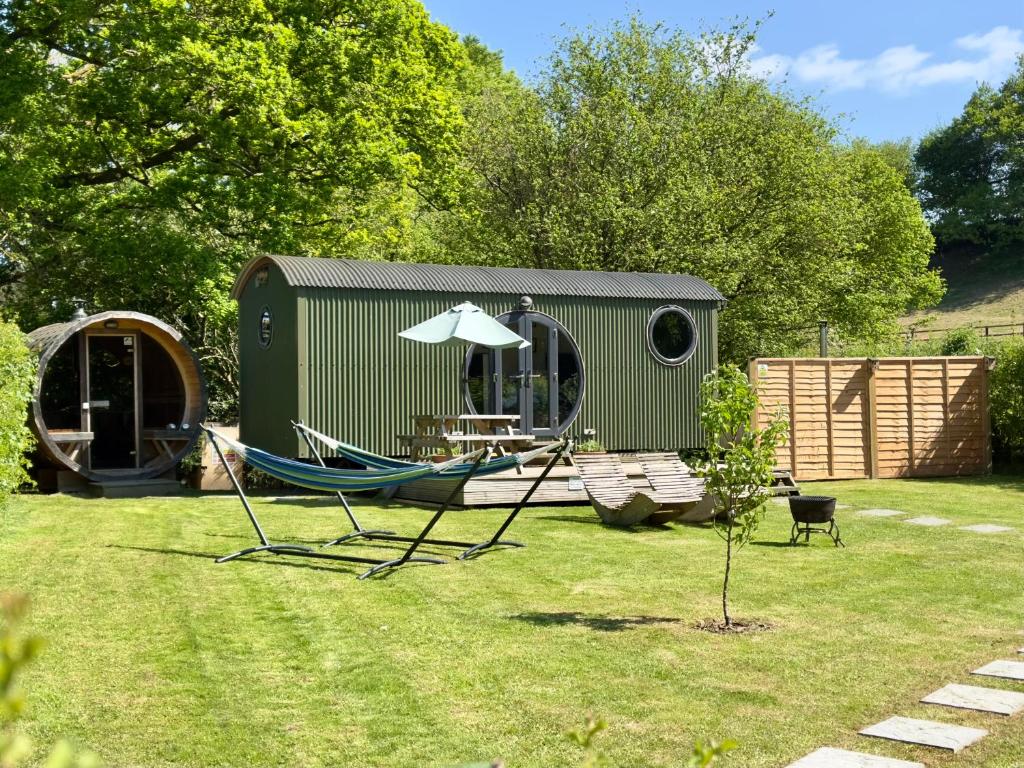 a hammock and an umbrella in a yard with a shed at The Shepherd's Hut at Hidden Wood Glamping in Corsley