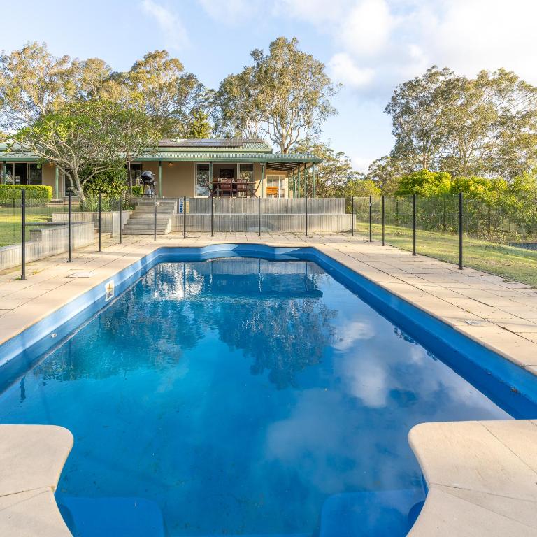 a pool with blue water in front of a house at Mara Luxe Farm Stay 20 mins from Beach in Forster
