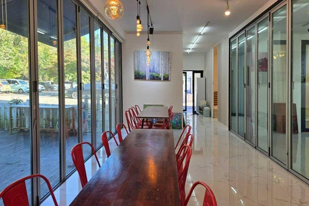 a dining room with a wooden table and red chairs at Paju Gallery Café Pension Soon in Paju