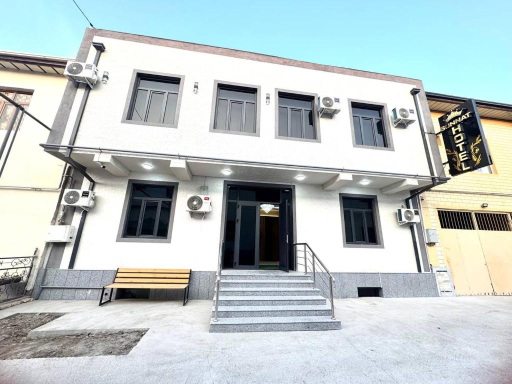 ein weißes Gebäude mit einer Bank davor in der Unterkunft Sunnat guest house in Buxoro