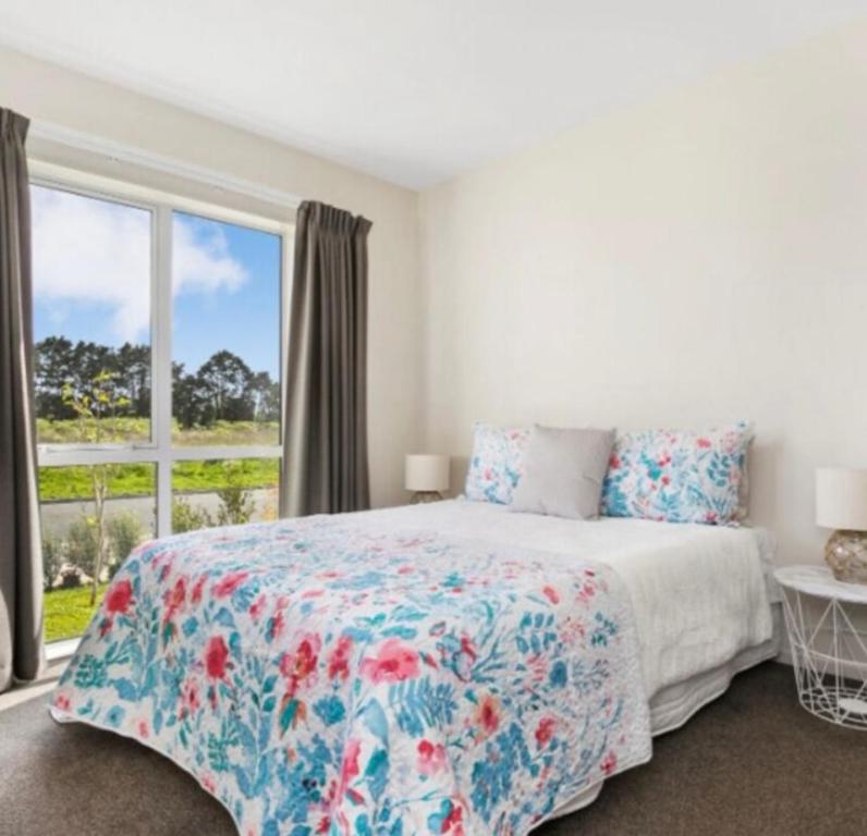 a bedroom with a bed with a floral bedspread and a window at Cozy Ensuite Room in Auckland