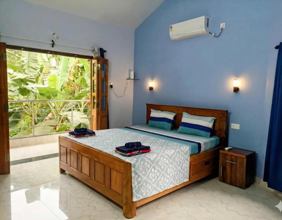 a bedroom with a bed with blue walls and a window at Roque's Place Goa in Betalbatim