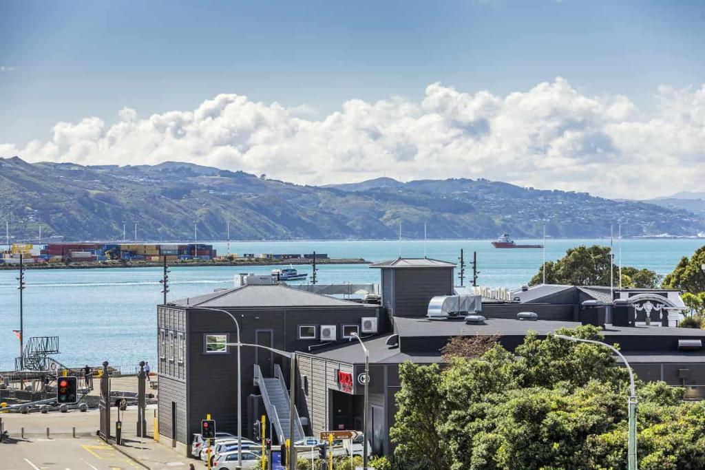 a building next to a body of water with mountains at 3-Bedroom CBD Elevate Apartment in Wellington