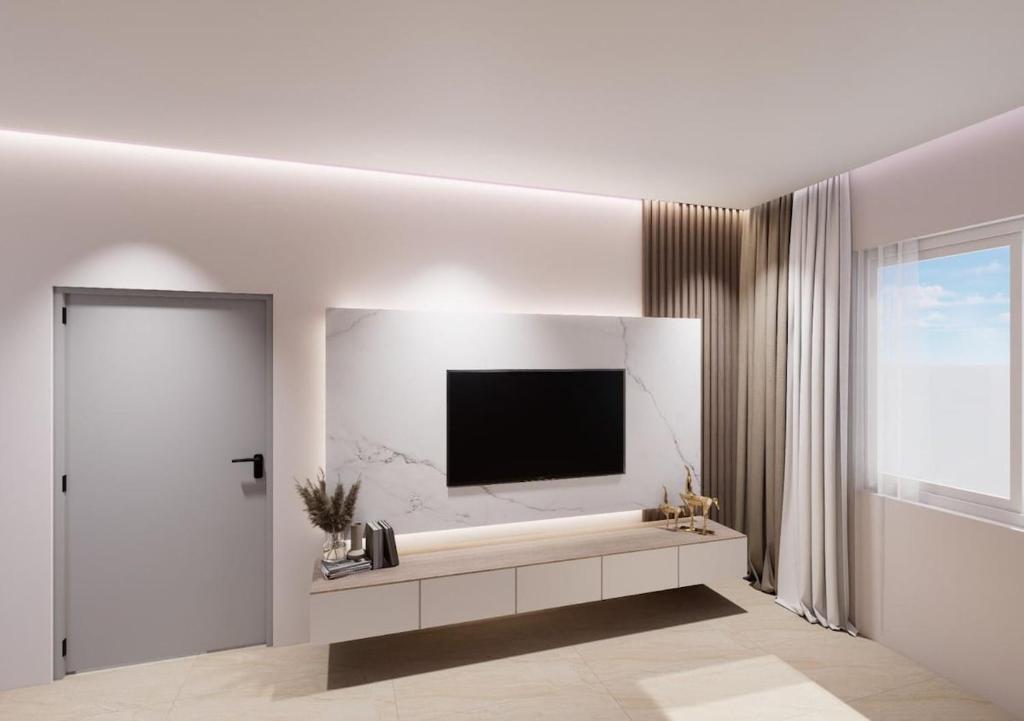 een witte woonkamer met een televisie aan de muur bij Havens Apartamen in Durrës