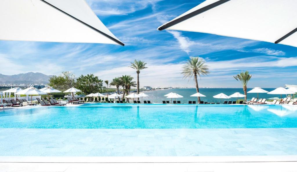 a swimming pool with white umbrellas and the ocean at Crowne Plaza Muscat by IHG in Muscat