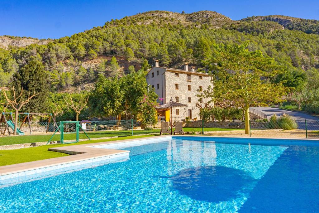 a large blue swimming pool with a building in the background at El Molinet del Governador- Apartamentos Rurales in Guadalest