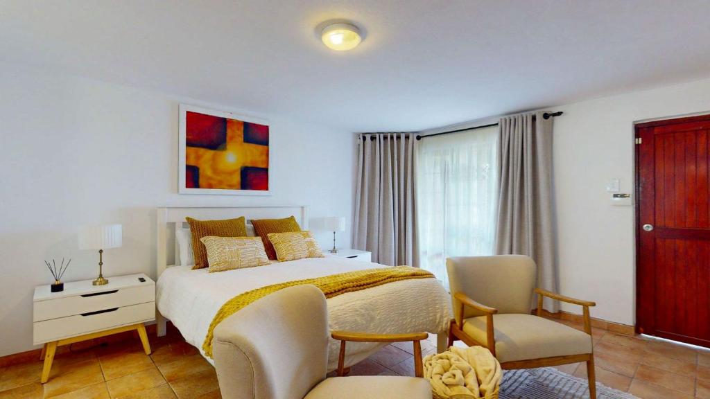 a bedroom with a bed and two chairs and a window at Guernsey Flat in Port Shepstone