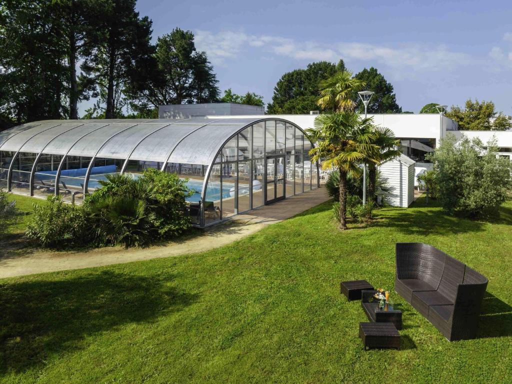 a large glass building with a pool in a yard at Novotel Nantes Carquefou in Carquefou