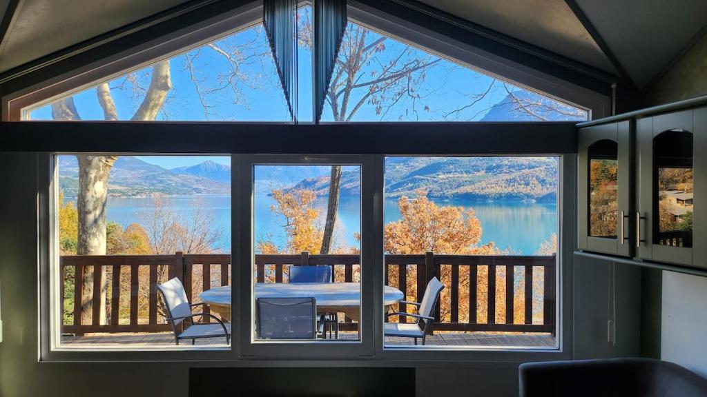 ein großes Fenster in einem Zimmer mit einem Tisch und Stühlen in der Unterkunft La perle du lac - Némausa location in Chorges