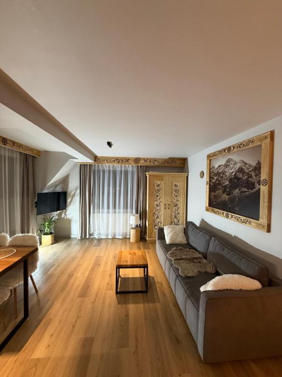 GÓRALSKIE NOWE APARTAMENTY BIAŁKA - Skibus, Sauny, Bania, Sale zabaw - w cenie في بيالكا تاترزانسكا: غرفة معيشة بها أريكة وطاولة
