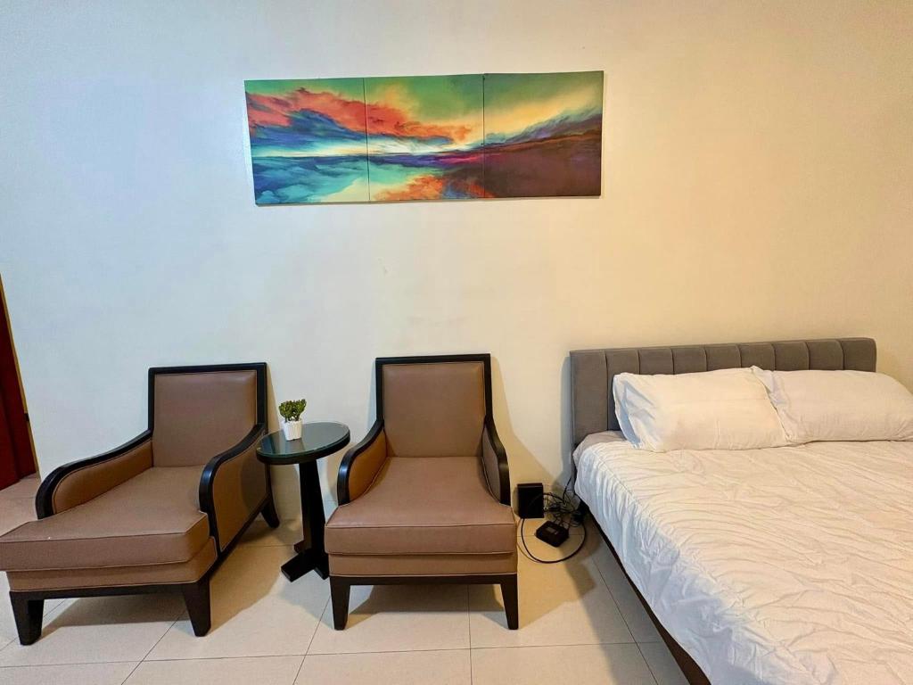 a bedroom with a bed and two chairs and a table at The Infinity Condominium BGC at high Street in Sampong