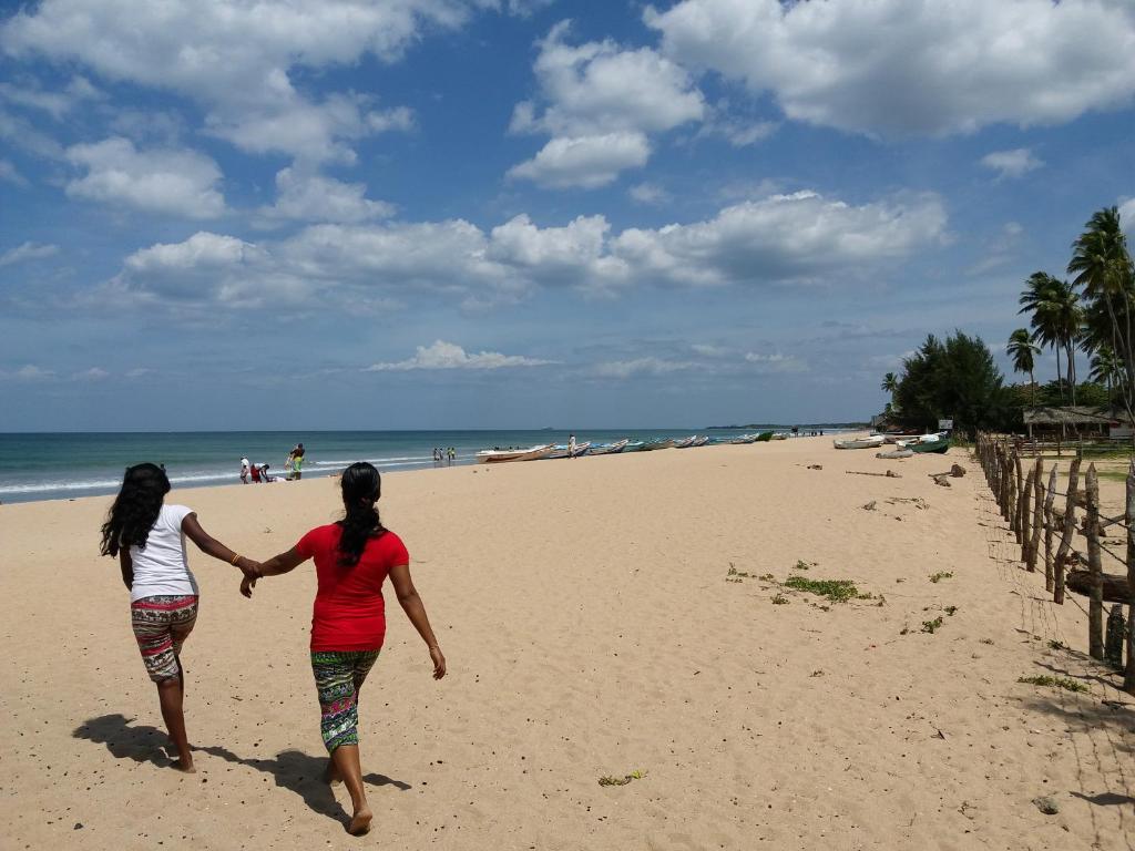 dos mujeres caminando en la playa tomadas de la mano en Marine Tourist Guest House at Negombo Beach en Negombo