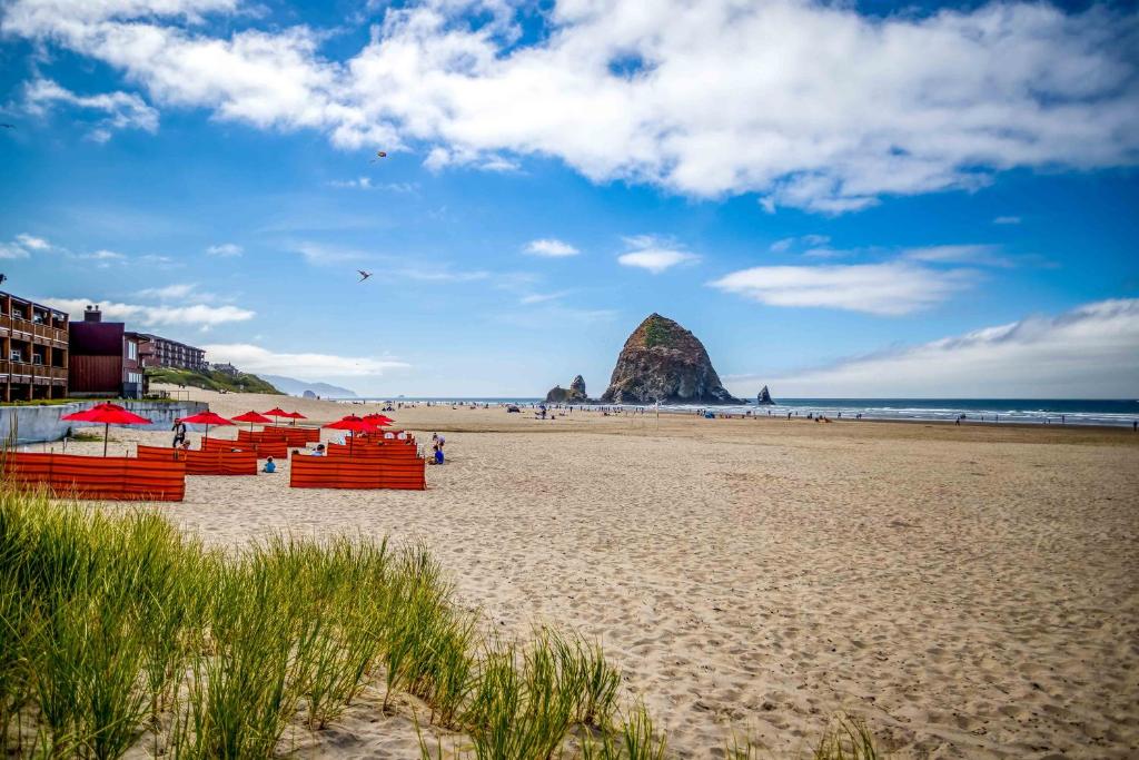 a beach with red chairs and a rock in the ocean at Cathys Cottage in Cannon Beach