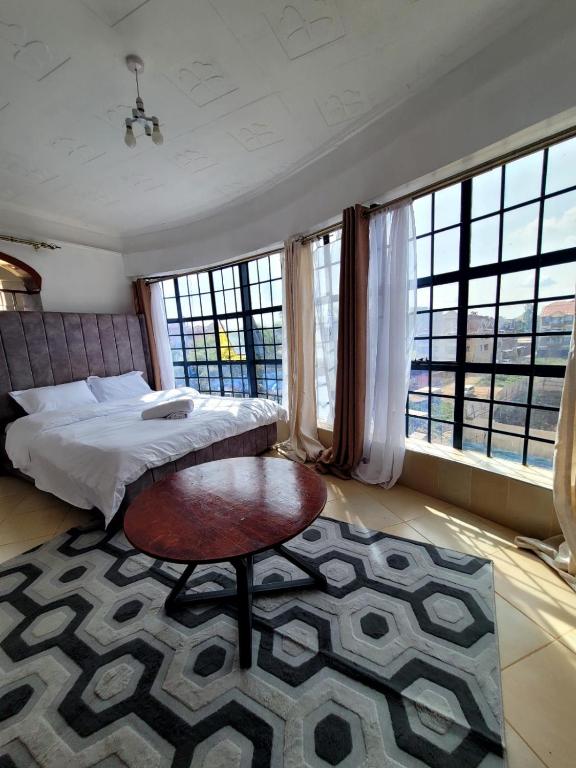 a bedroom with a bed and a table and windows at Serene63 Studios Kenol,Muranga in Gitura