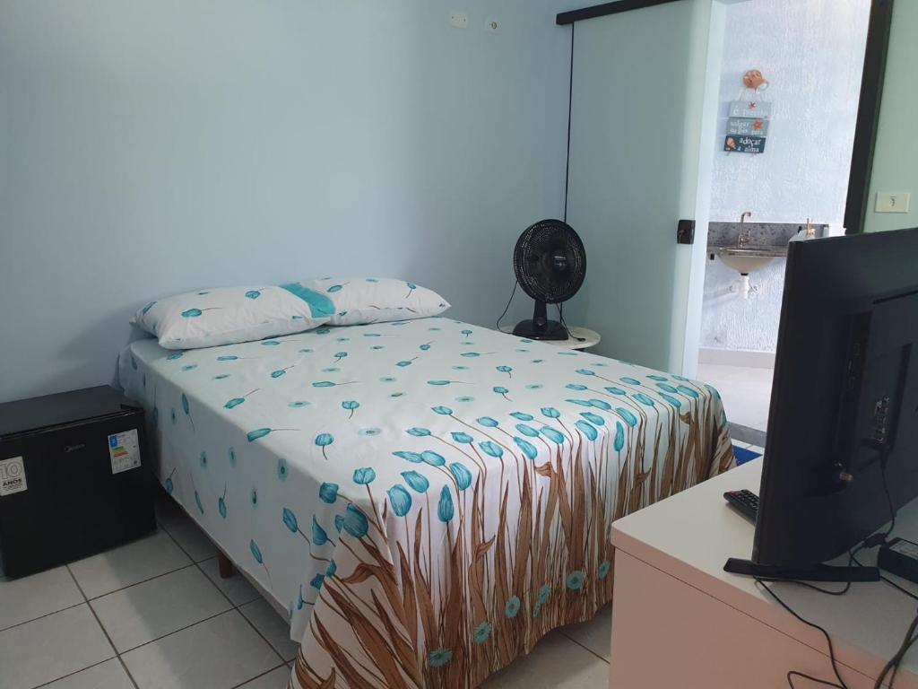 a bedroom with a bed and a desk with a television at suite confortavel temporada caraguatatuba in Caraguatatuba