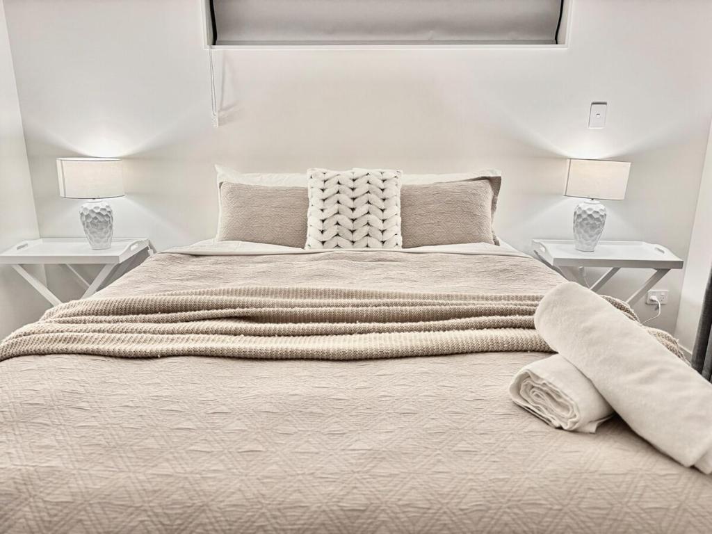 a white bedroom with a large bed with two tables at New 4BR Family Home in Greenhill Park, Chartwell in Hamilton