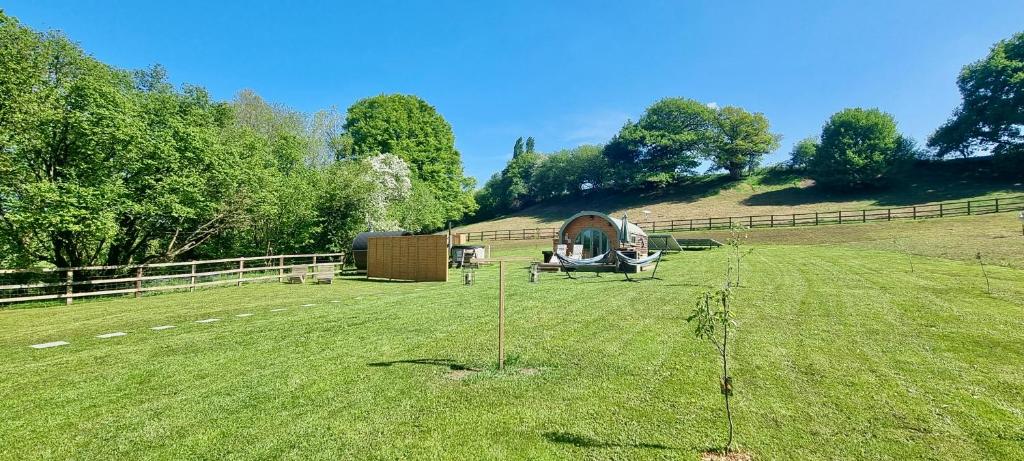 a large grass field with a building on a hill at The Mainstay Pod at Hidden Wood Glamping in Corsley