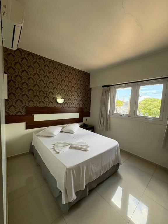 a bedroom with a white bed and two windows at Hotel Boa Vista - 200mts do Shopping Pátio in Chapecó