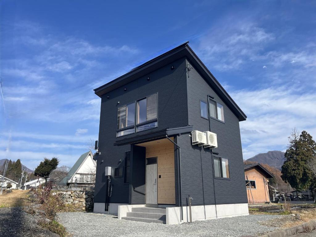 a black house with a white door on a street at Hakuba Icicle House in Hakuba