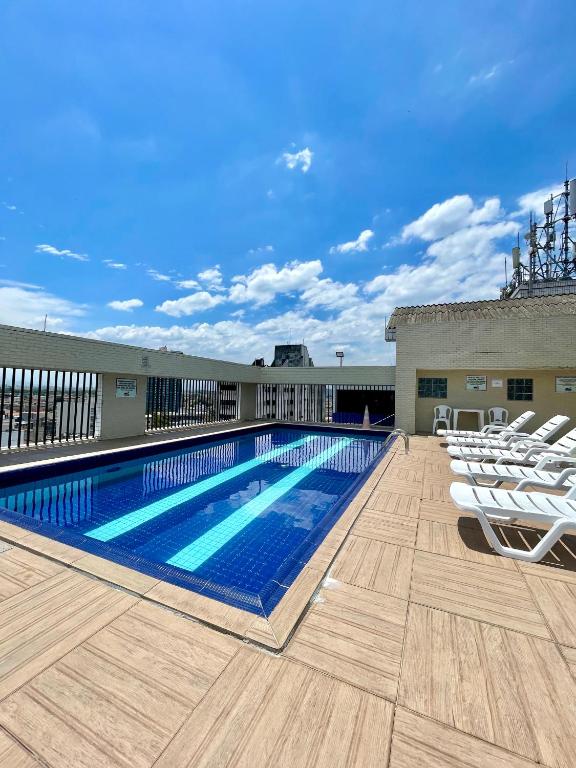 a swimming pool on the roof of a building with white chairs at Palladium Prime Stay in São Vicente