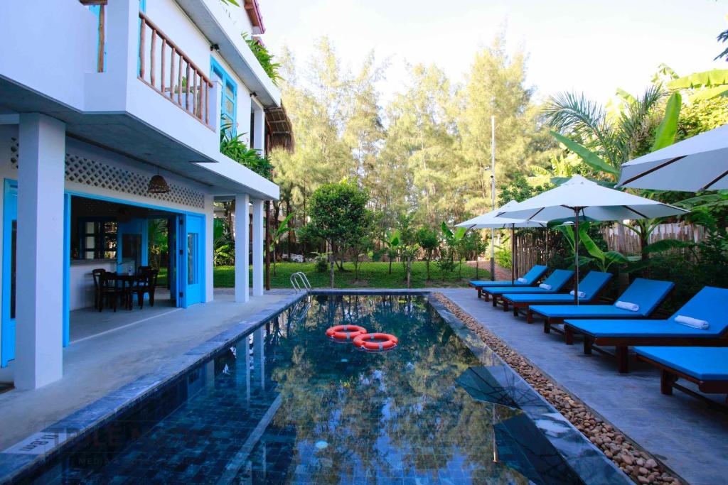 a pool with chairs and umbrellas next to a house at Life Beach Villa in Hoi An