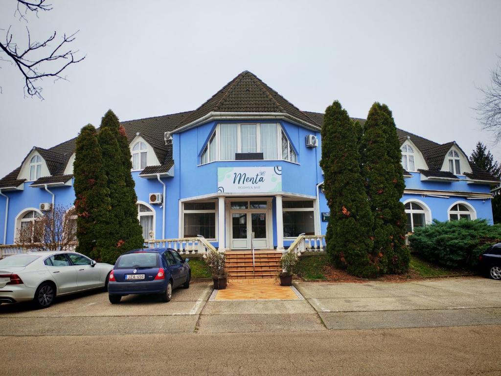 a blue house with cars parked in front of it at Menta Rooms & Bar in Kapuvár
