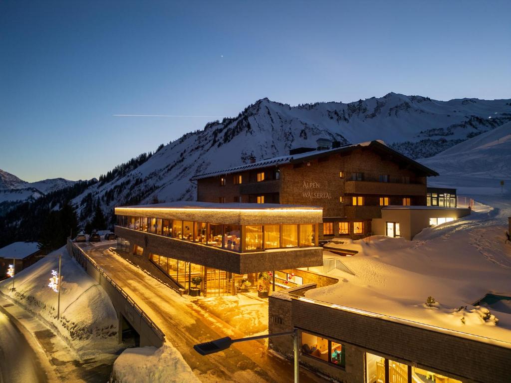 a building in the snow with mountains in the background at Alpenresort Walsertal in Damuls