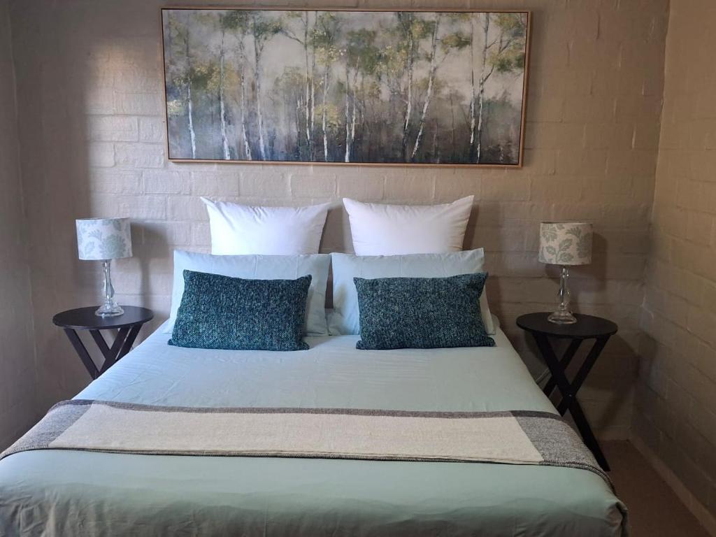 een bed met blauwe kussens en een schilderij erboven bij 5Viooltjiestraat in Riversdale