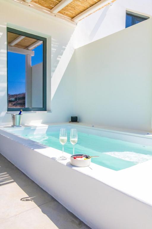 a pool with two wine glasses and a bowl of food at Rockaine Suites Sunset in Agios Fokas